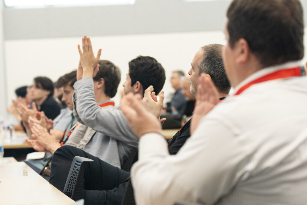 Audience members seated in rows applaud during a presentation.