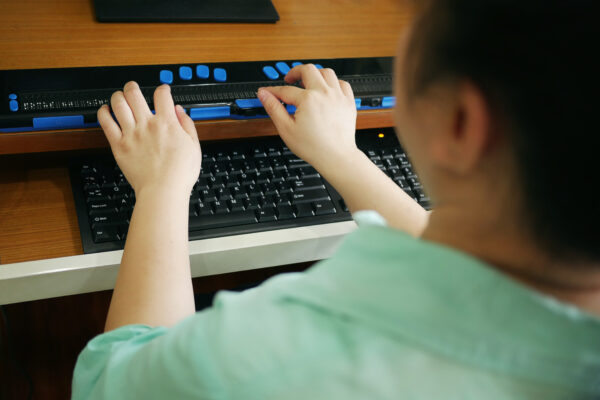 A person with blindness using a technology assistive device for persons with visual impairment