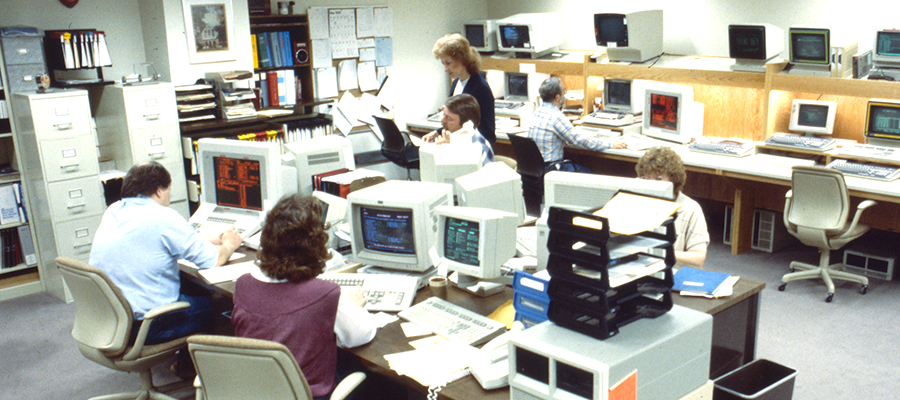 A group of people work at computers in an office in the 1990s