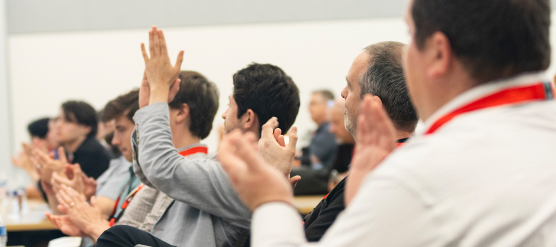 Audience members seated in rows applaud during a presentation.