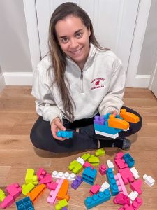 Dariane Drake, a woman with long brown hair, plays with large, colorful building blocks on the floor.