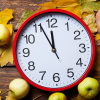 Red clock on a table with fall colored leaves, apples, and a pumpkin.