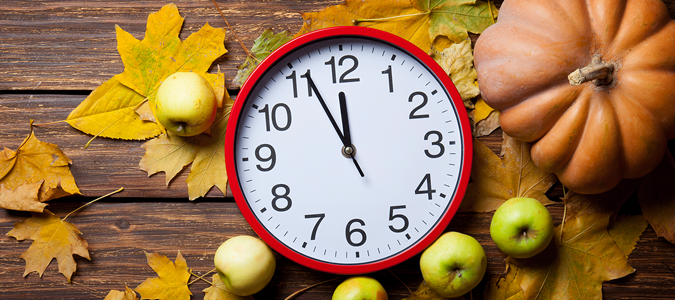 Red clock on a table with fall colored leaves, apples, and a pumpkin.