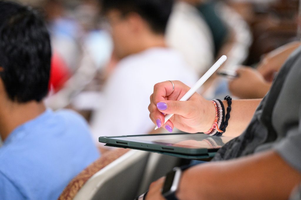 A student writes notes on a tablet on the first day of class