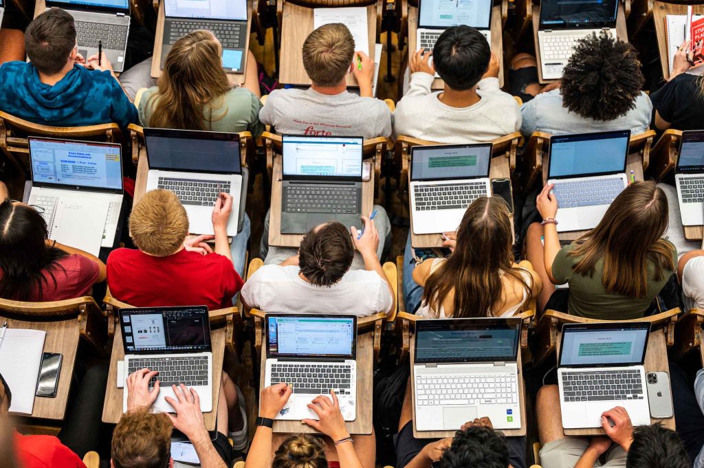 Students sit in rows of desks with laptops open