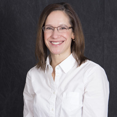Laura Grady, a caucasian woman in her late 40s with shoulder-length brown hair, glasses, wearing a white button-down shirt.