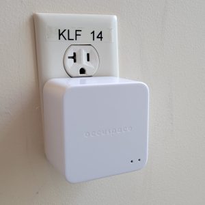 A white, square device plugged into a wall outlet with the word "Occuspace" written on it.