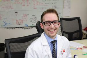 Photo of Ryan Werner at the DoIT Help Desk wearing his School of Pharmacy white lab coat