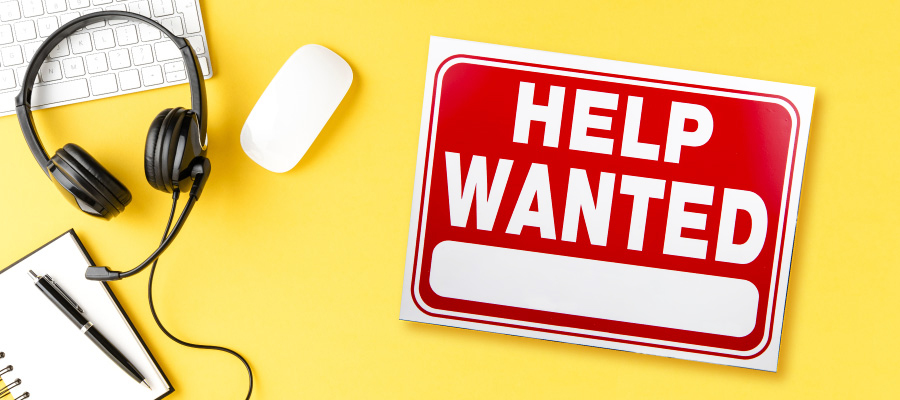 Keyboard, a headset, mouse, and note pad next to a "Help Wanted" sign