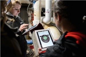 students with tablets in a room full of pipes and equipment