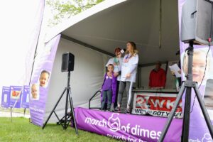 Corissa Runde holds a microphone on stage with her family at the 2019 Madison March for Babies